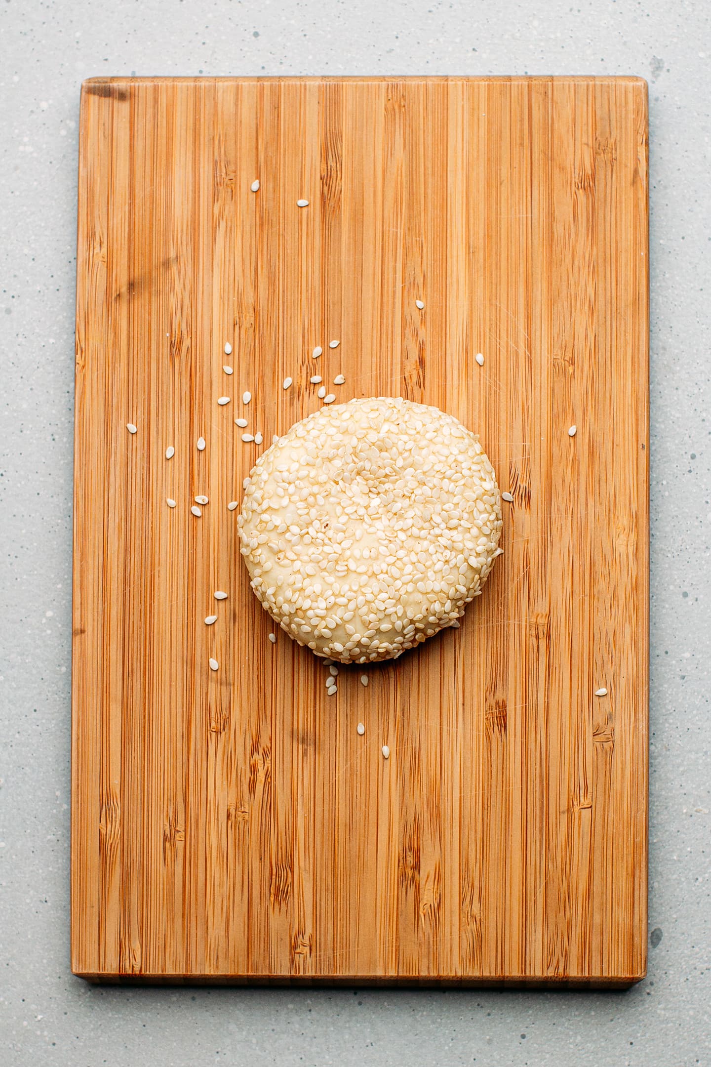 Ball of dough coated with sesame seeds on a cutting board.