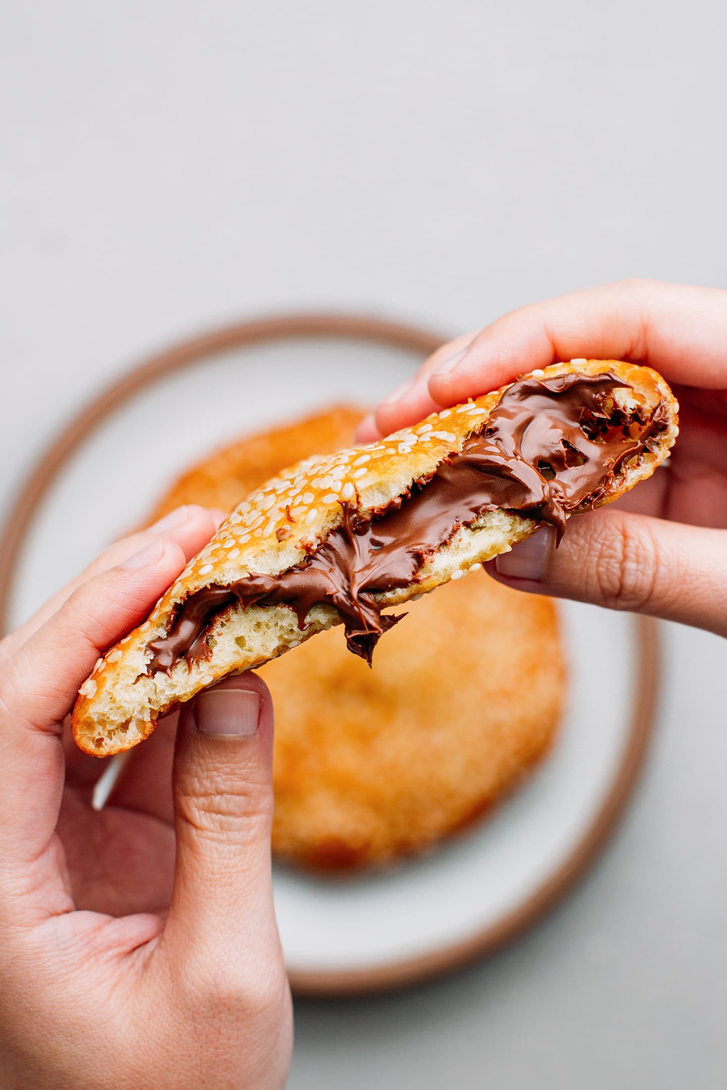 Holding sesame donut filled with chocolate spread.