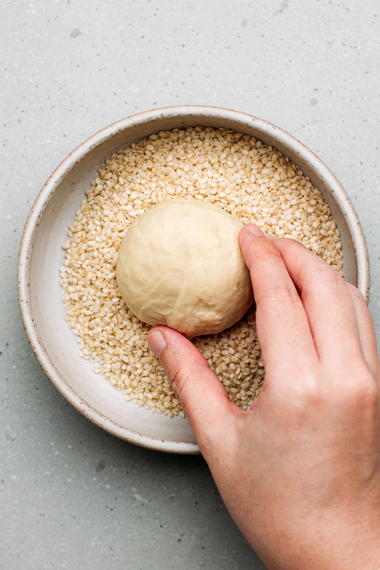 Dipping a ball of dough into sesame seeds.