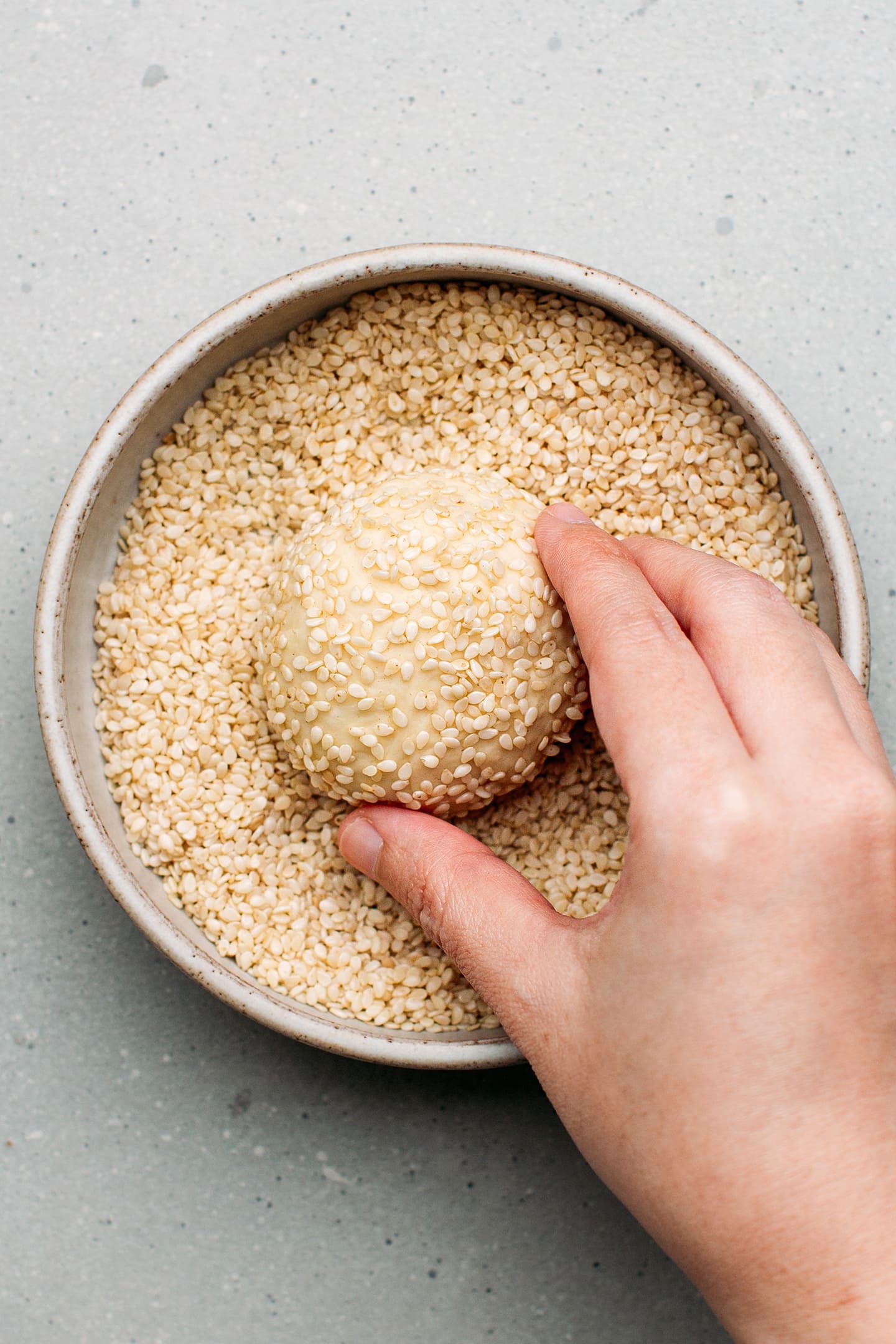 Coating a ball of dough with sesame seeds.