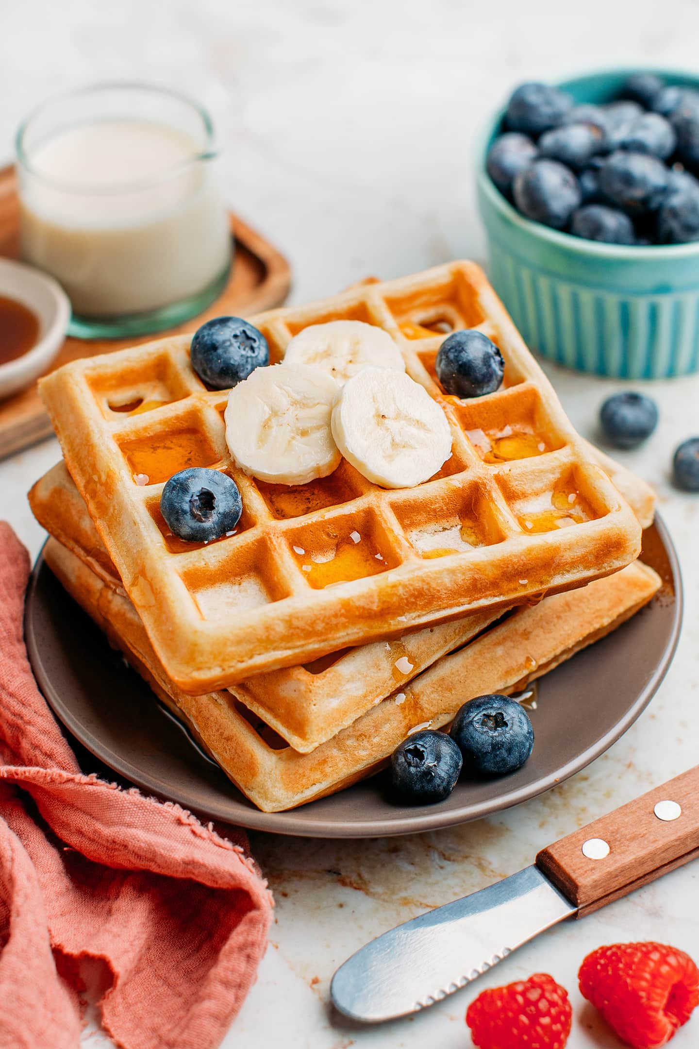 Vegan waffles topped with maple syrup, blueberries, and bananas.