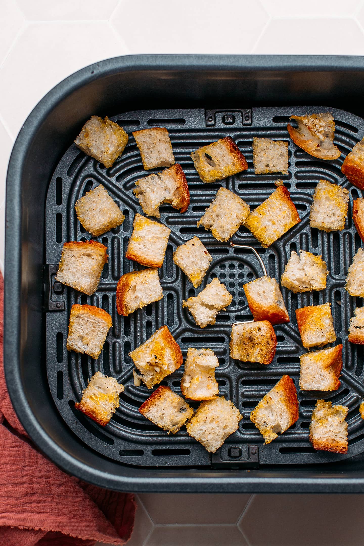 Uncooked croutons in the basket of an air fryer.