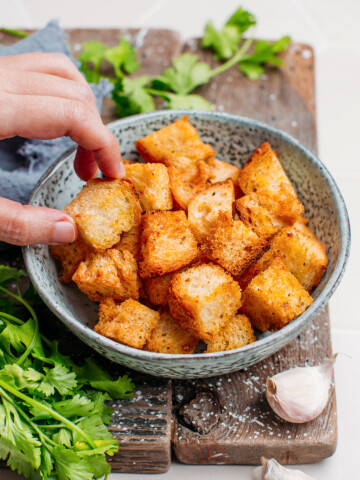 Hand holding a piece of crouton over a serving bowl.