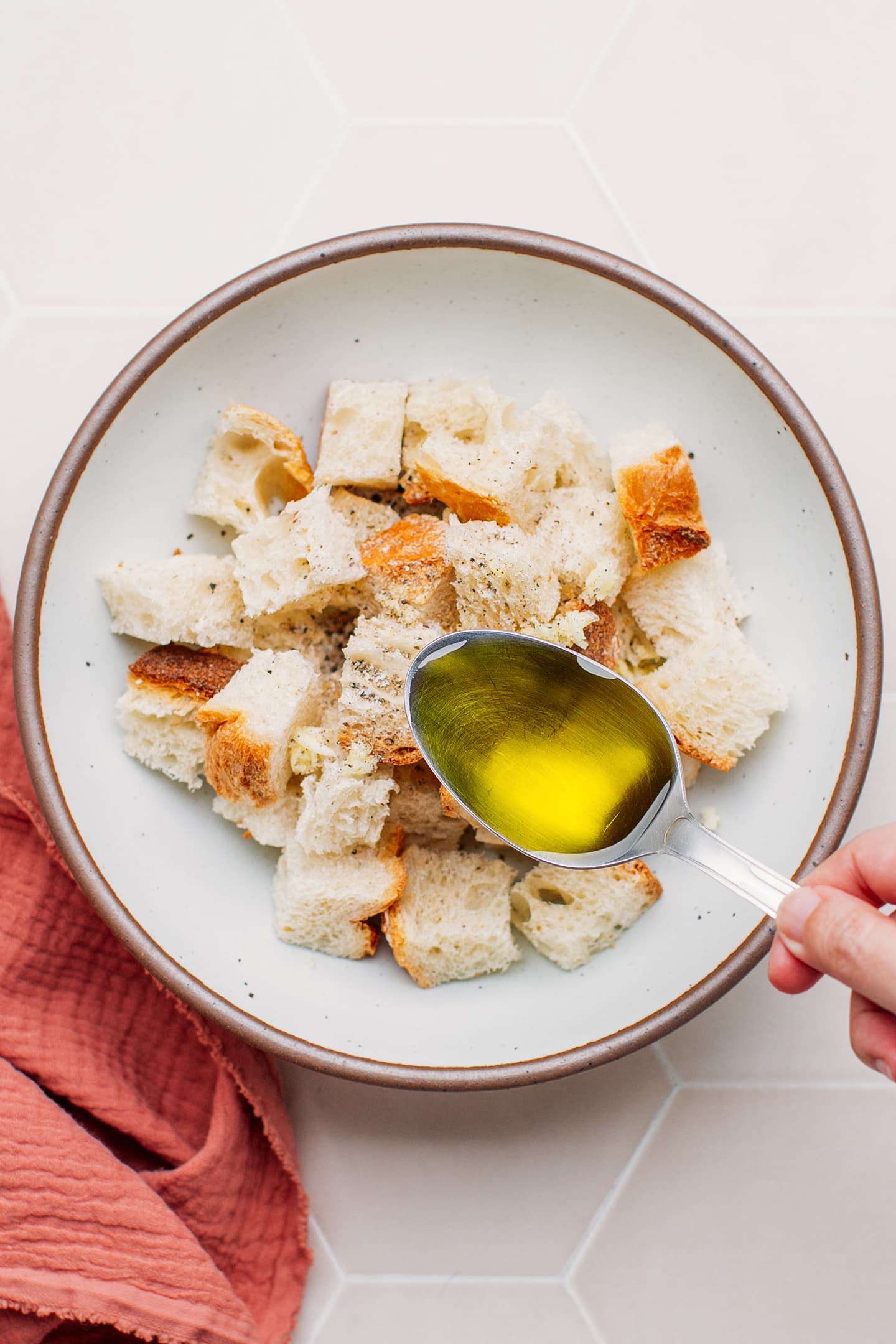 Pouring olive oil over diced bread.