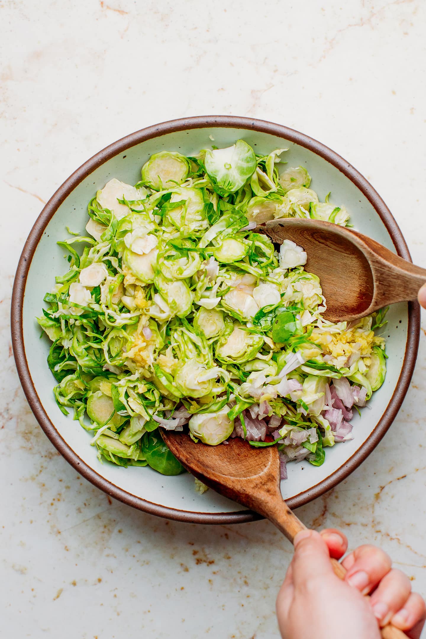 Tossing shaved Brussels sprouts with a dressing.