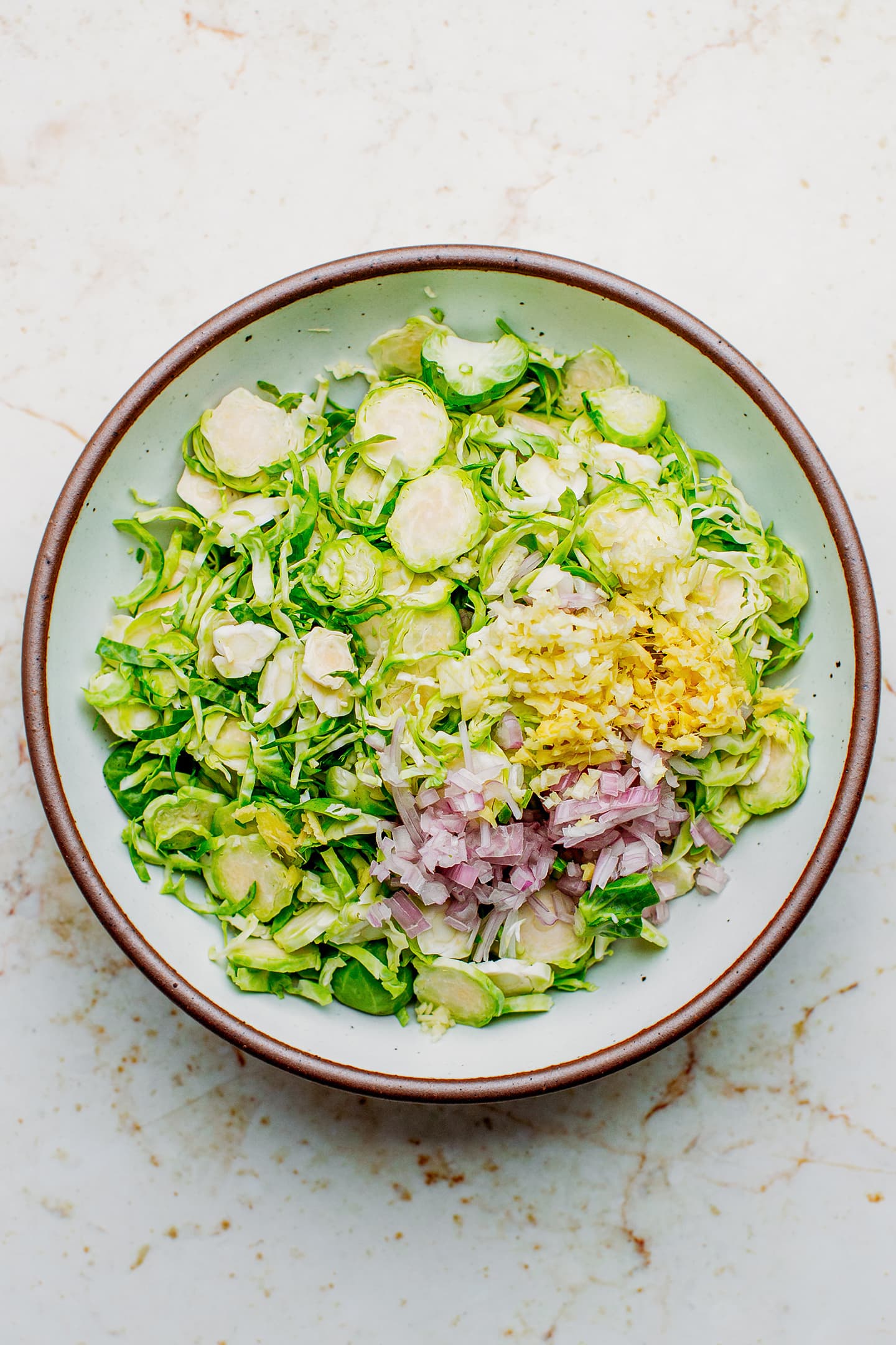 Shaved Brussels sprouts, ginger, shallots, and garlic in a bowl.