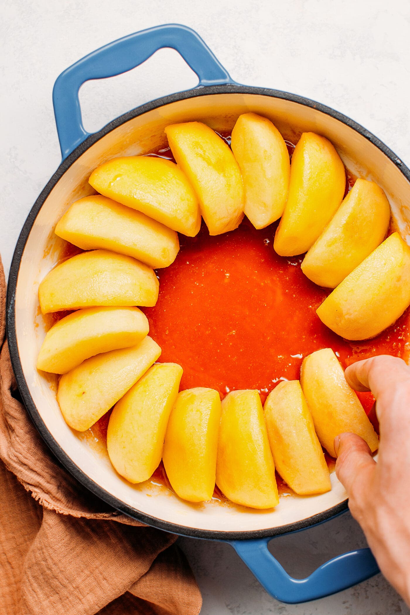 Arranging apple slices on top of caramel, in a pan.