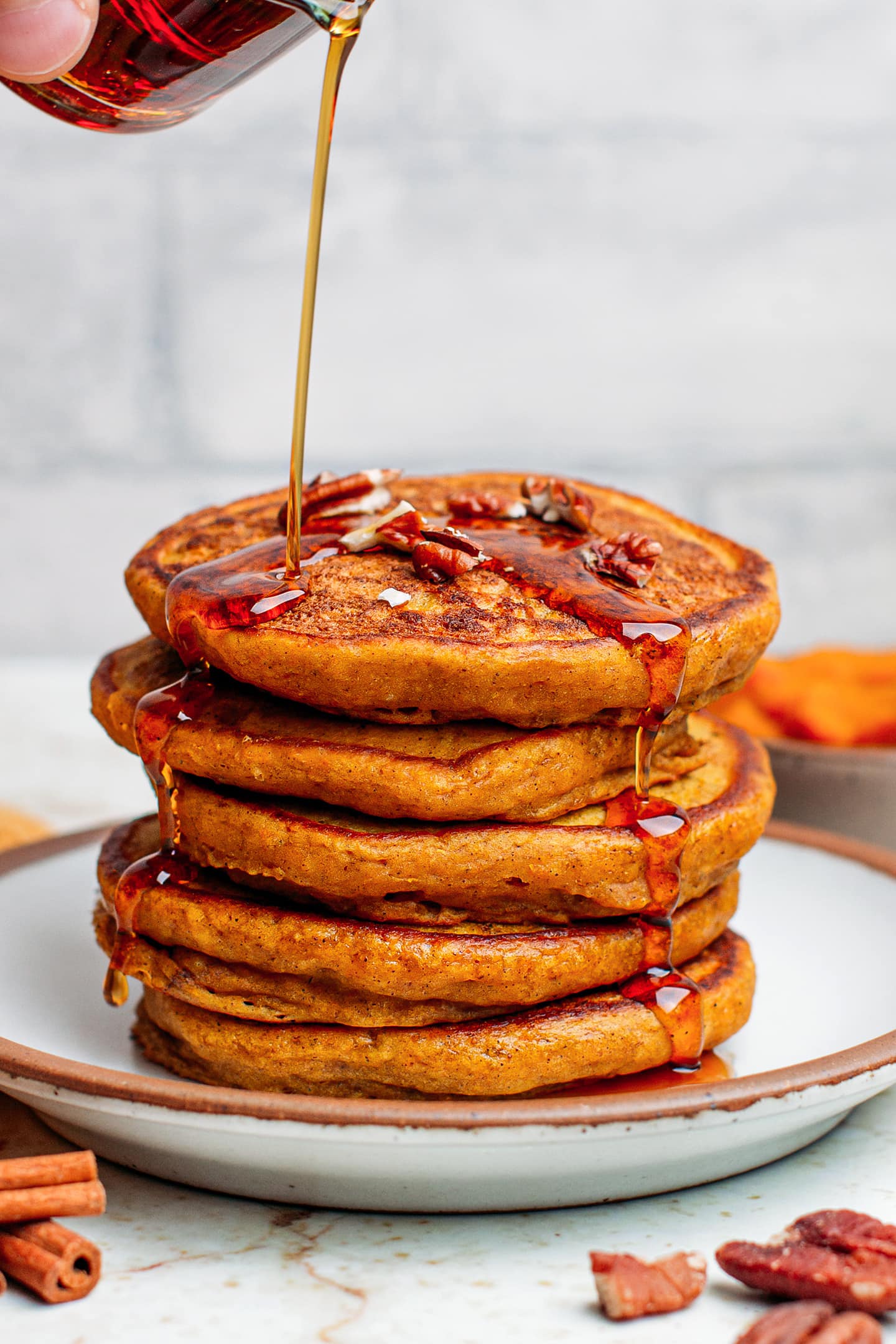 Pumpkin pancakes stack topped with maple syrup and crushed pecans.