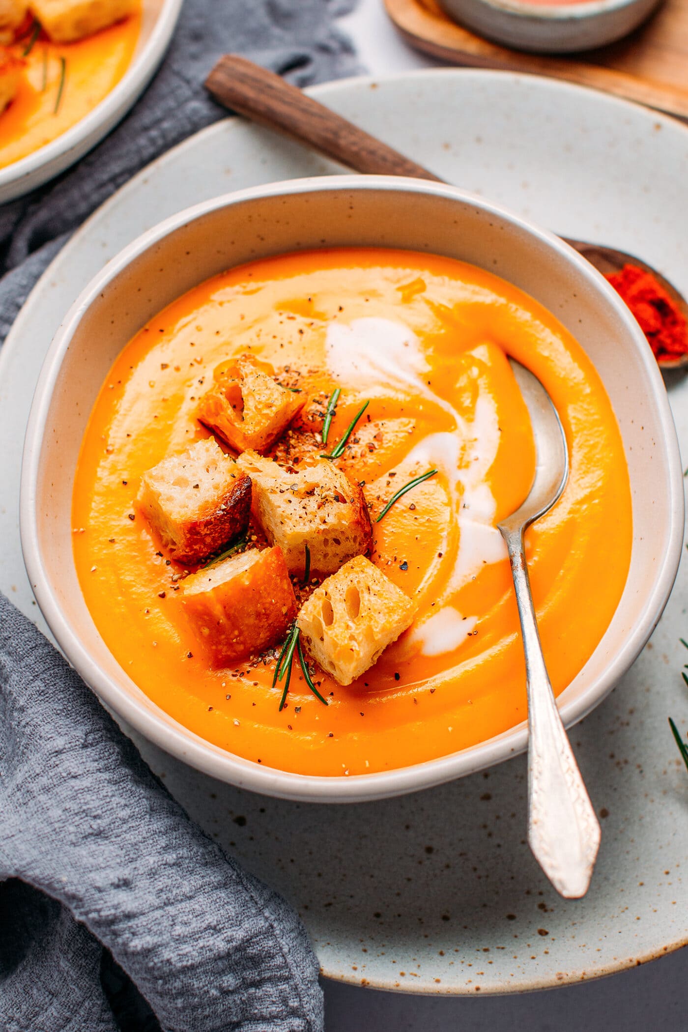 Bowl of sweet potato soup topped with croutons and rosemary.