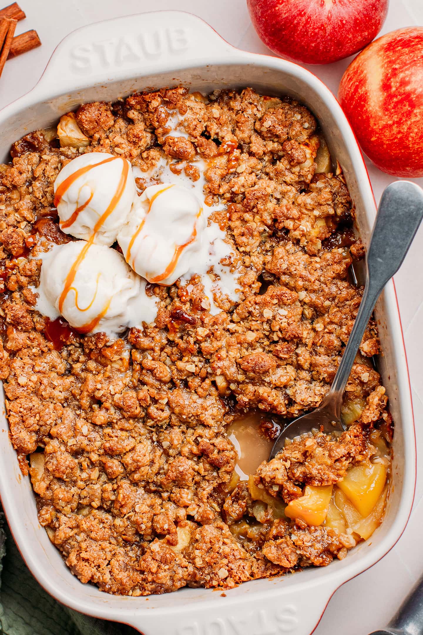 Apple crisp topped with scoops of vanilla ice cream and caramel sauce.