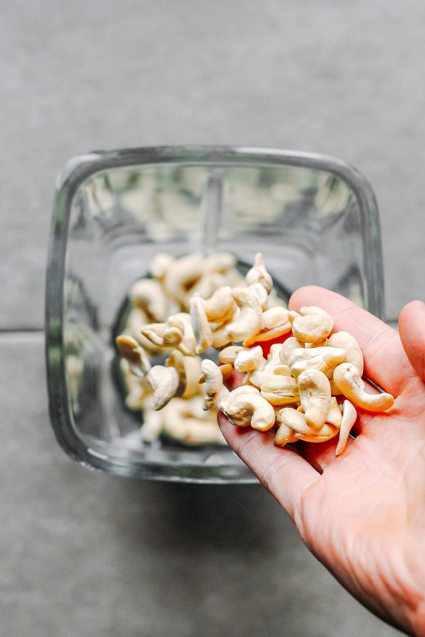 Adding cashews to the bowl of a blender.