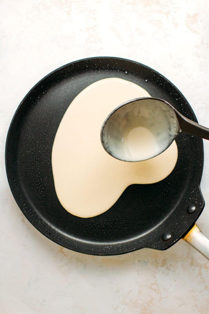 Pouring crêpe batter in a skillet.