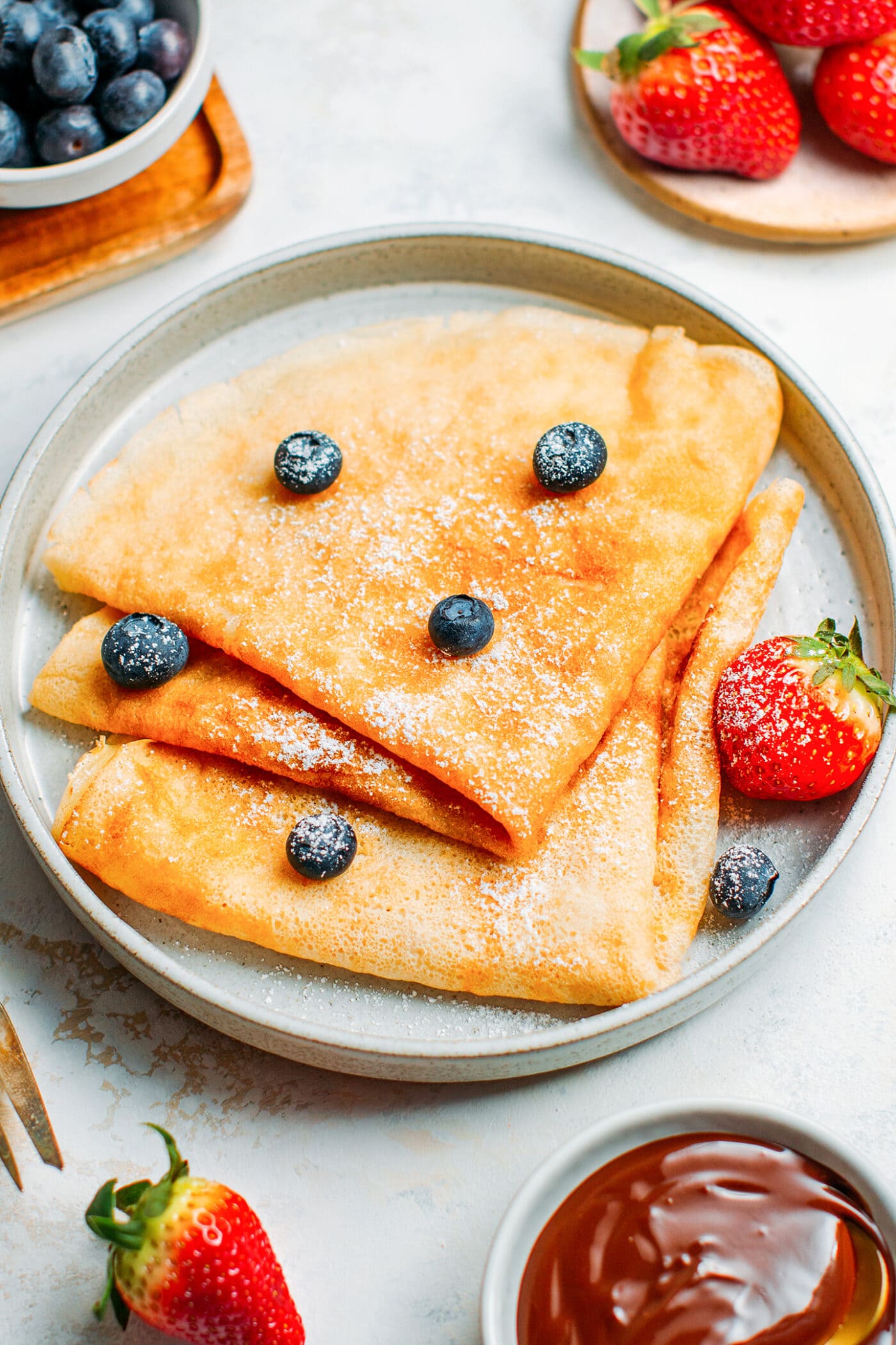 Vegan French crêpes with powdered sugar, blueberries, and strawberries.