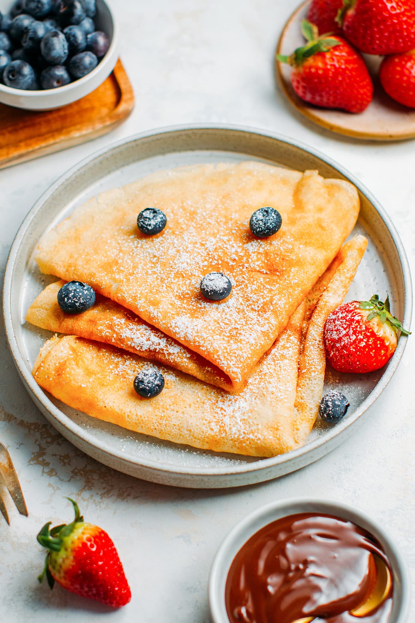 Vegan crêpes topped with powdered sugar, blueberries, and strawberries.