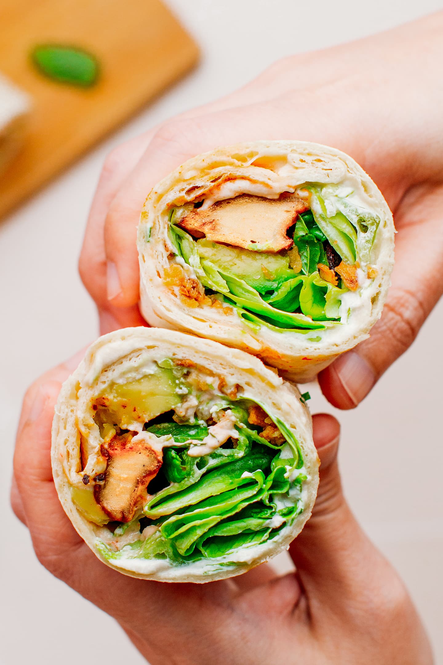 Holding two wraps with vegan chicken, lettuce, and avocado.