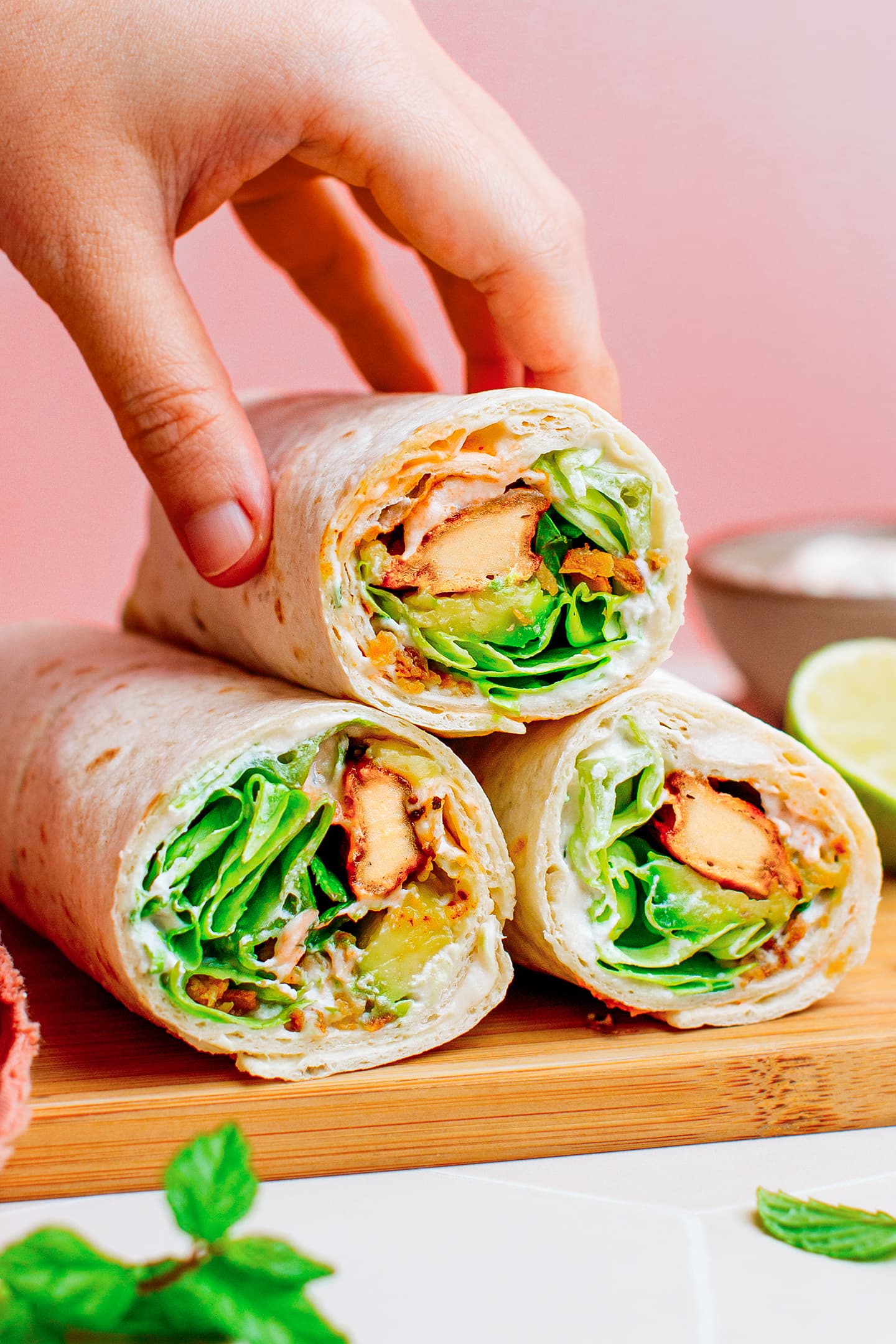 Holding a vegan wrap filled with vegan chicken, cream cheese, and lettuce.