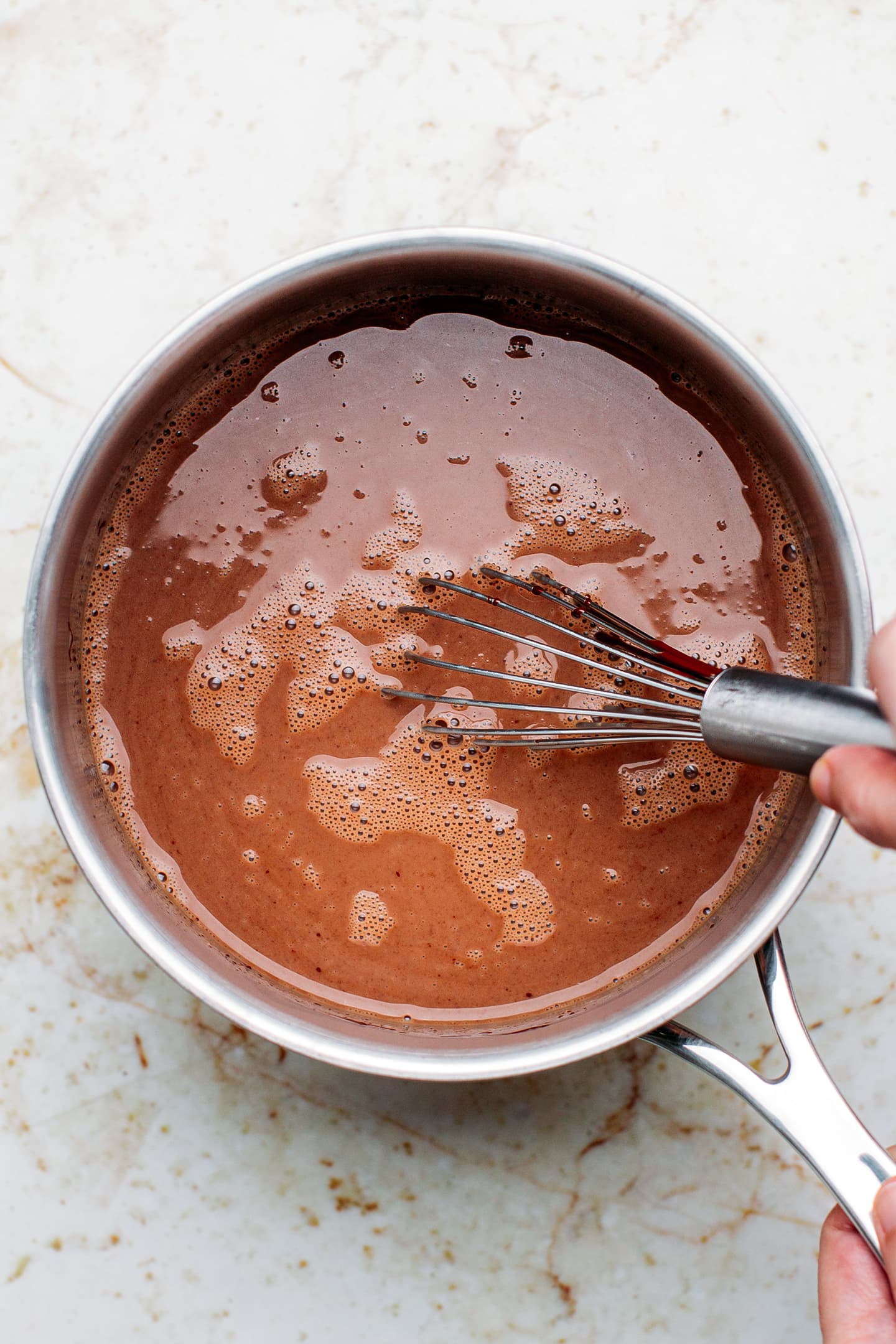Whisking melted chocolate and milk in a saucepan.