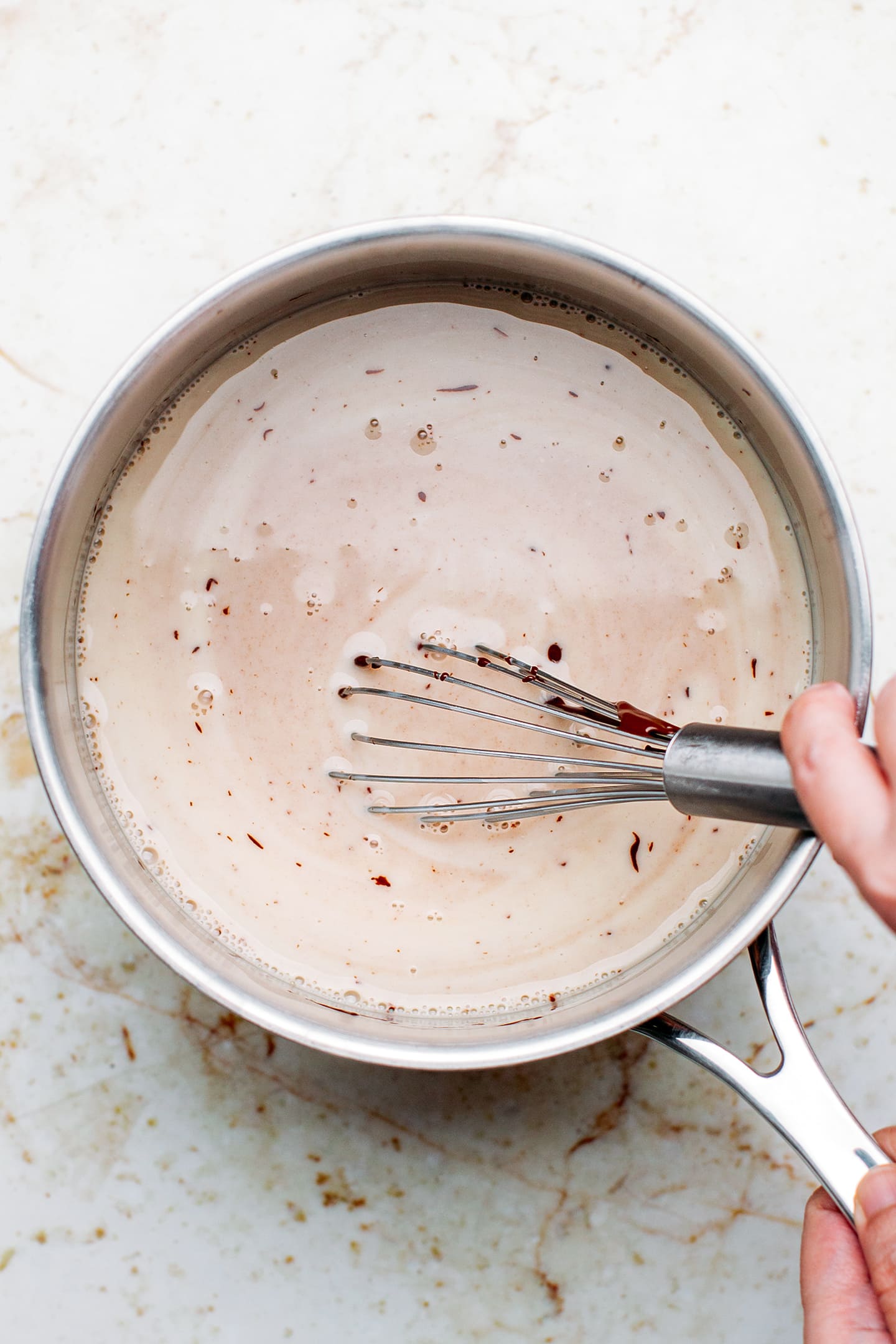 Whisking melted dark chocolate and milk in a saucepan.