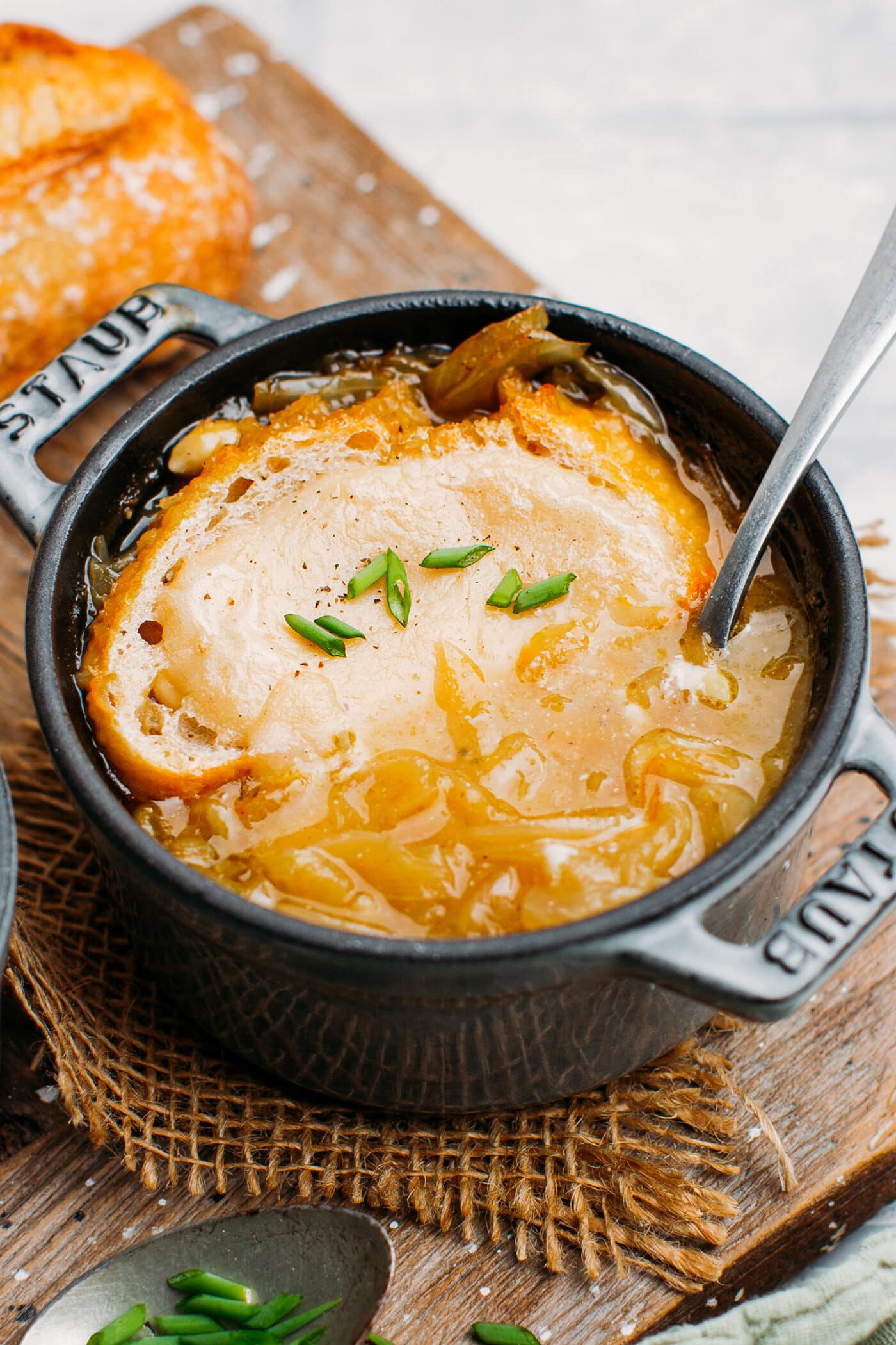 Close up of vegan onion soup with bread, cheese, and scallions in a pot.